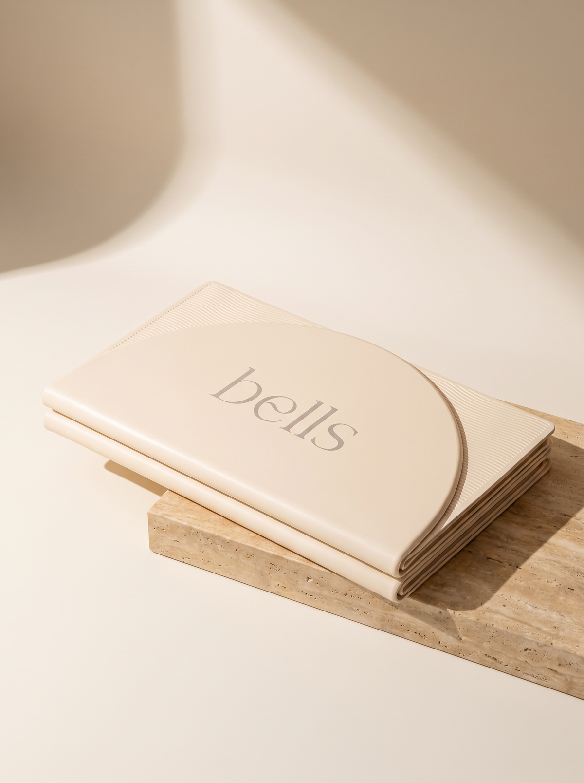 Bells Foldable Mat cream dobrado sobre bloco de travertino, luz do sol